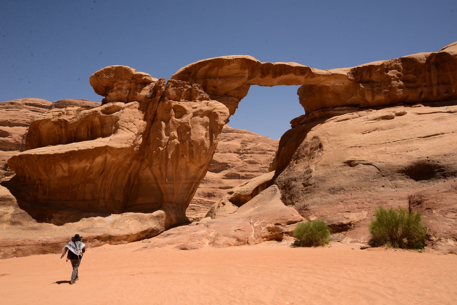 Man approaching an enormous stone arch at Wadi Rum in Jordan