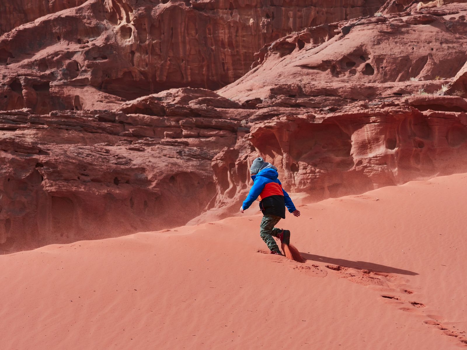 A child running down the red sand dunes of Wadi Rum in Jordan