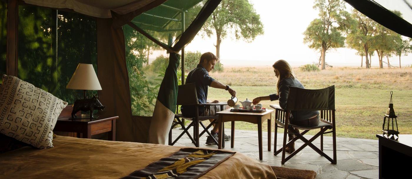 A couple sitting having tea at the front of their luxury tent at Governors Camp in Kenya