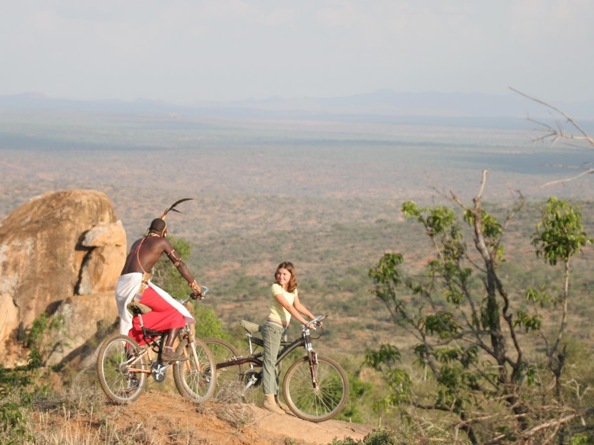 a guests and Masai guide mountain biking through the African bush at luxury safari lodge Lodo Springs in the Laikipia region of Kenya
