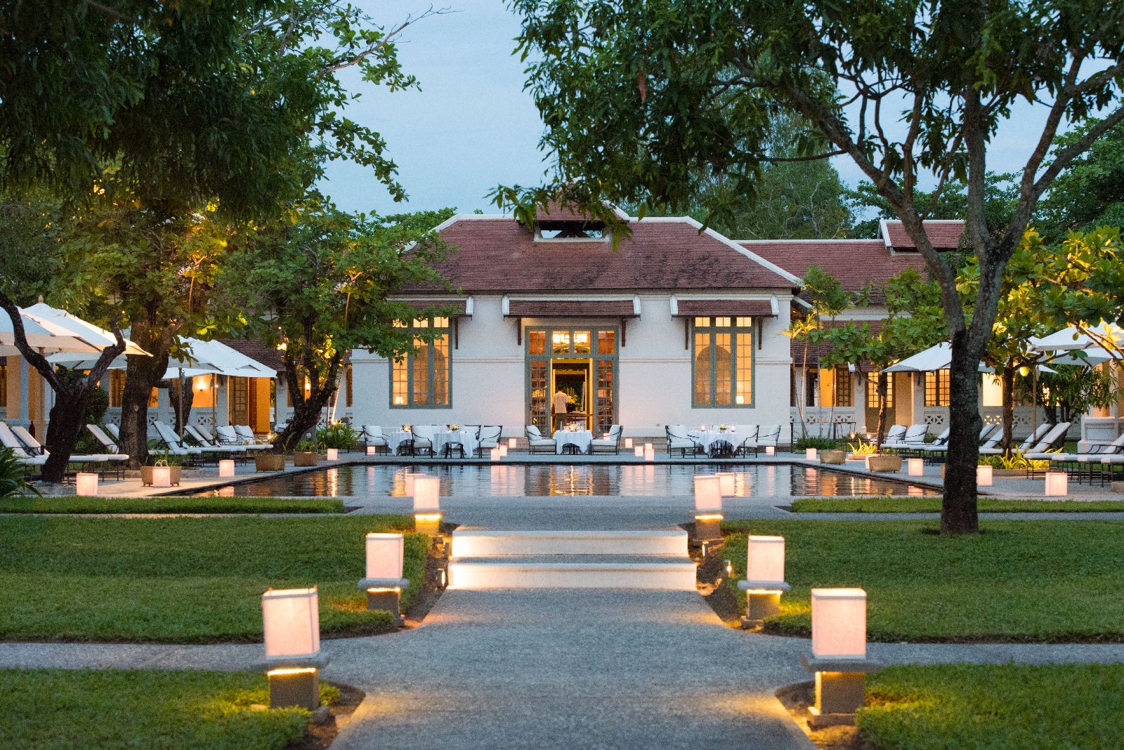 The pool and grounds at Amantaka Laos lantern lit at dusk
