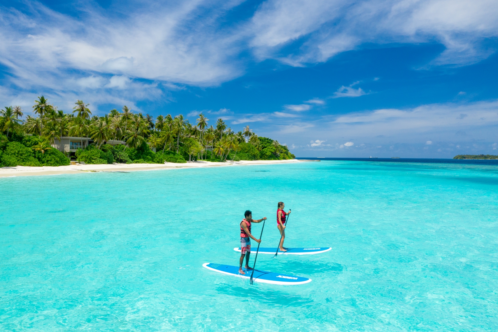 Two guests stand up paddling in the turquoise waters of the Indian Ocean at luxury resort Amilla in the Maldives