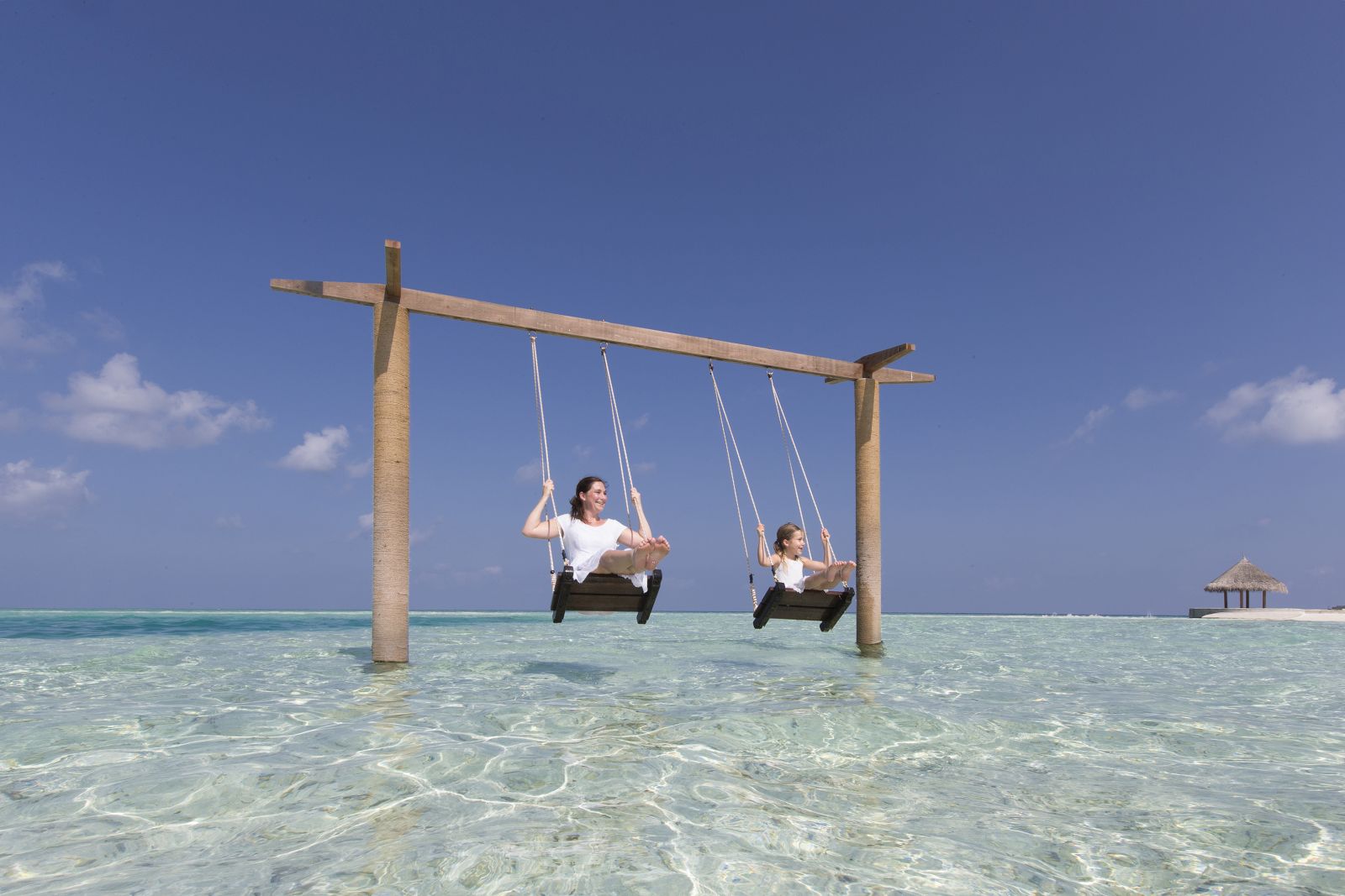 Two children swinging over the water on a beach swing at Anantara Dhigu in the Maldives