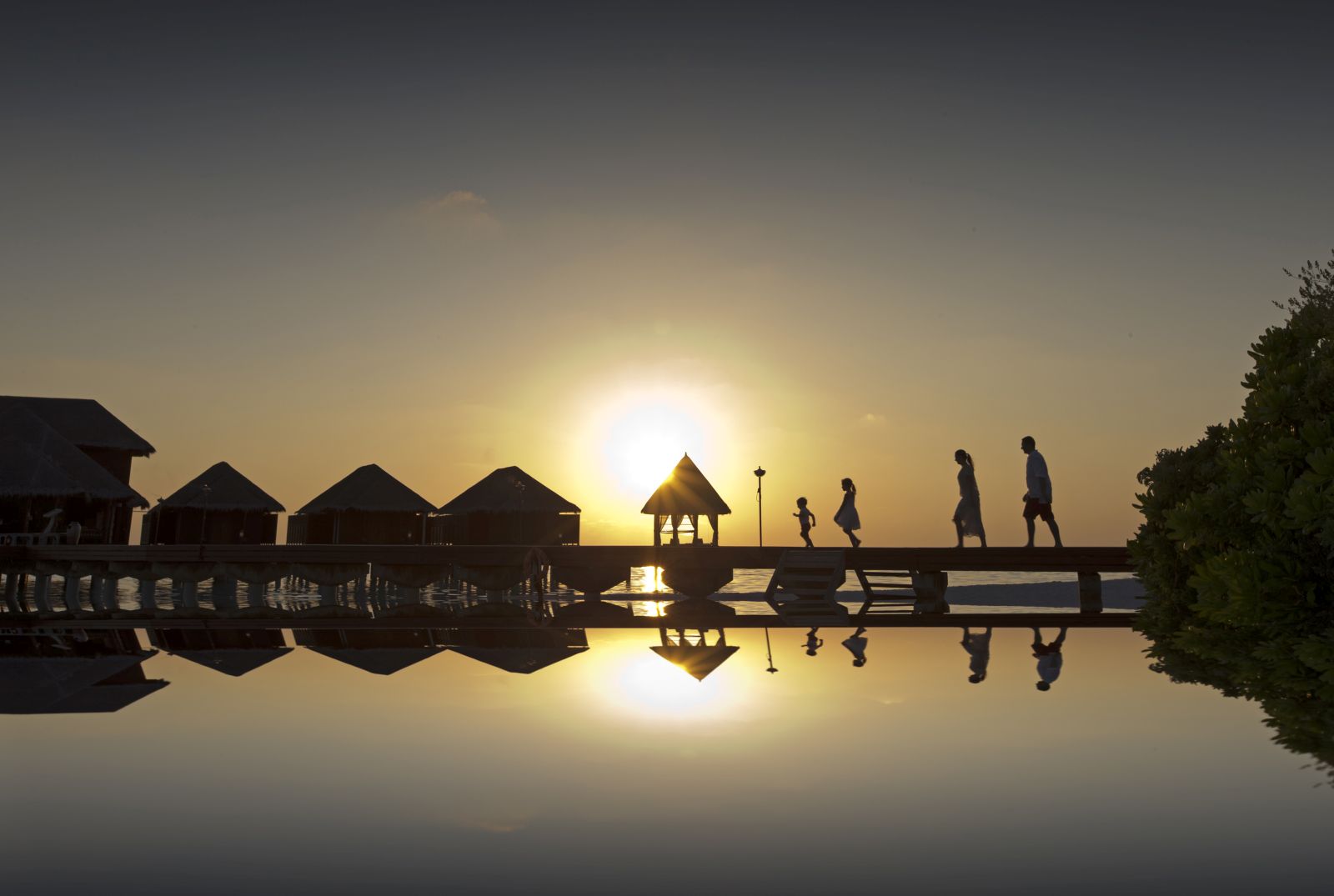 A family walking down the board walk at sunset at Anantara Dhigu in the Maldives