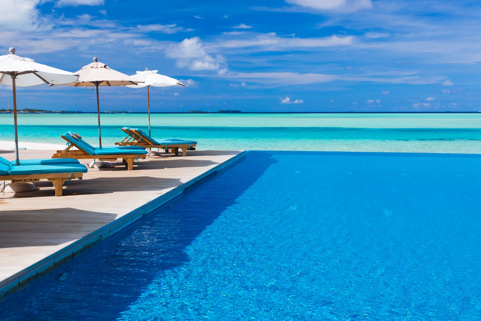 Sunloungers with umberellas by the side of the pool overlooking the ocean at Anantara Dhigu in the Maldives