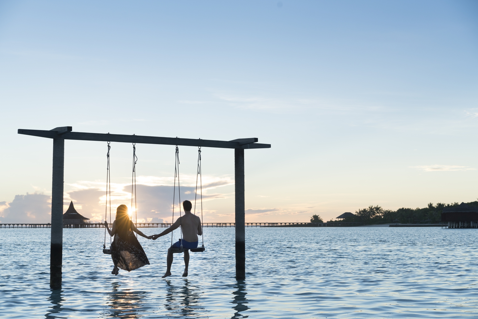 Couple watching sunset on an overwater swing at luxury resort Anantara Veli in the Maldives