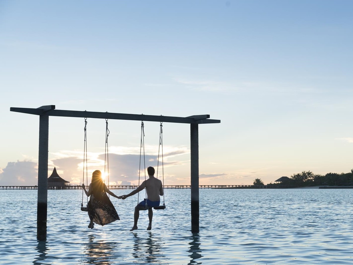 Couple watching sunset on an overwater swing at luxury resort Anantara Veli in the Maldives