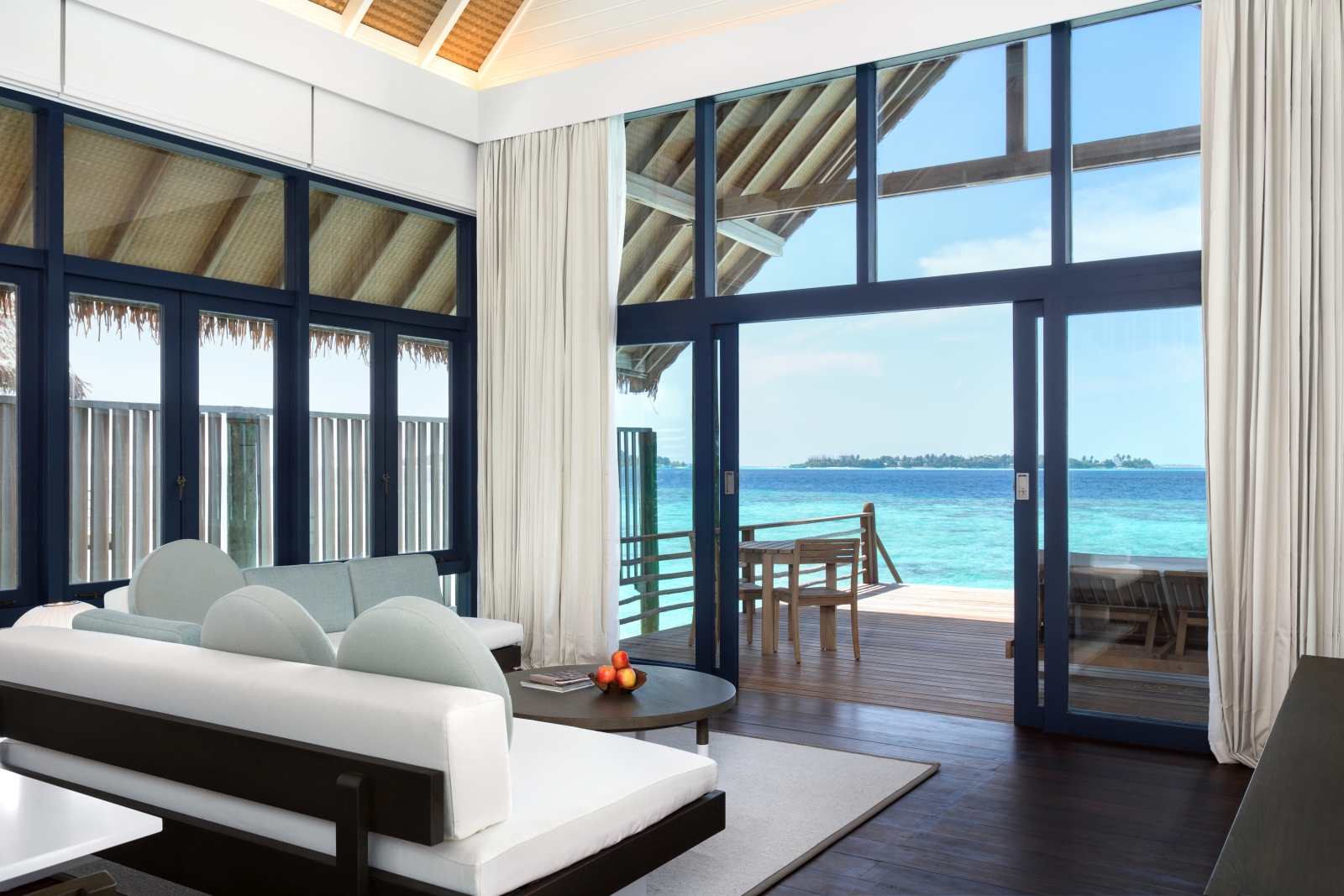 Looking out of the living room of a Loft Water Villa over the private deck and turquoise waters of the Indian Ocean at luxury resort Cocoa Island in the Maldives