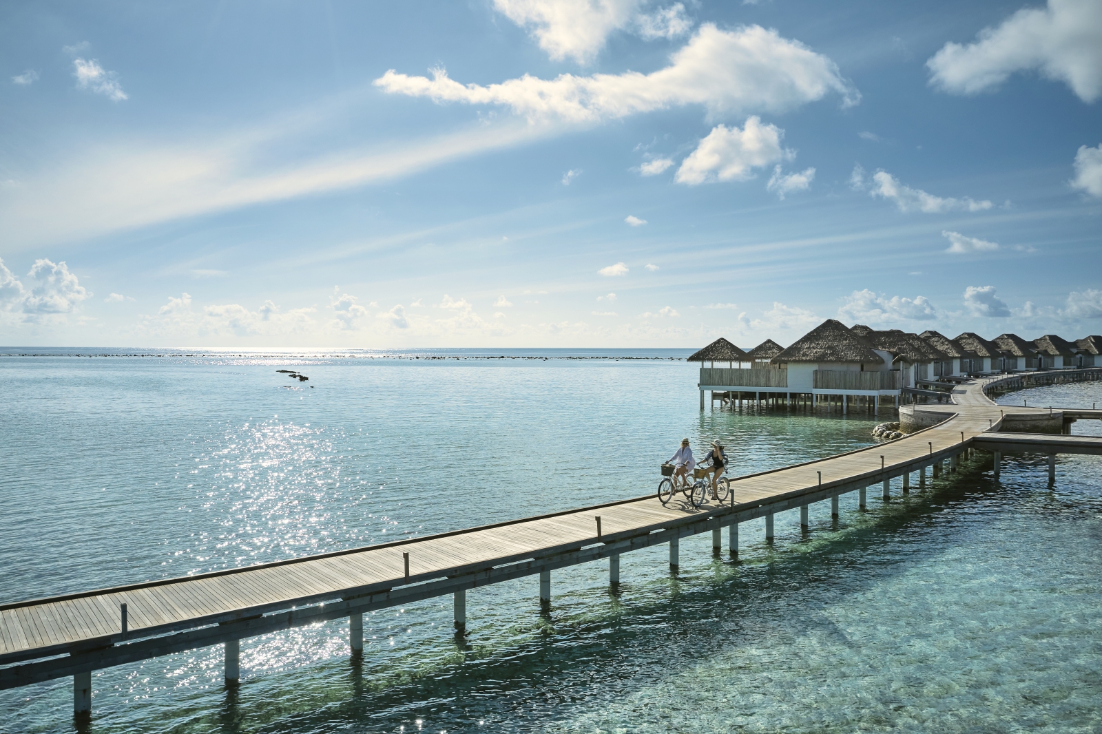 couple cycling down a jetty at luxury resort COMO Maalifushi in the Maldives