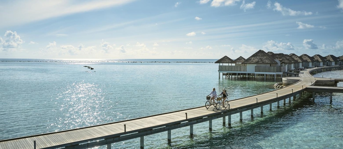 couple cycling down a jetty at luxury resort COMO Maalifushi in the Maldives