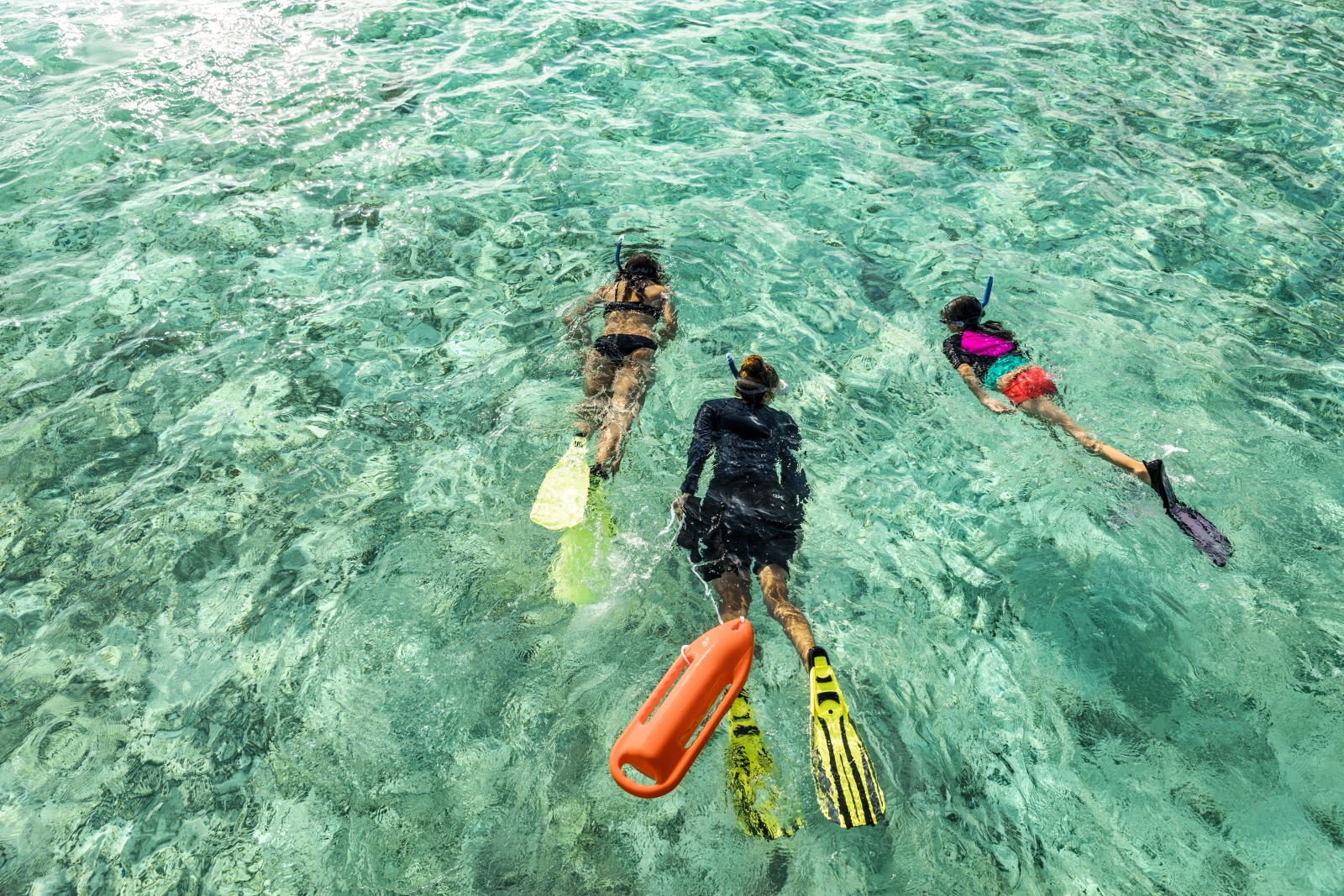 Family snorkelling in the turquoise waters of the Indian Ocean at luxury resort COMO Maalifushi in the Maldives