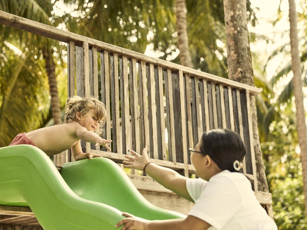 Staff member playing with child on the playground at luxury resort COMO Maalifushi in the Maldives