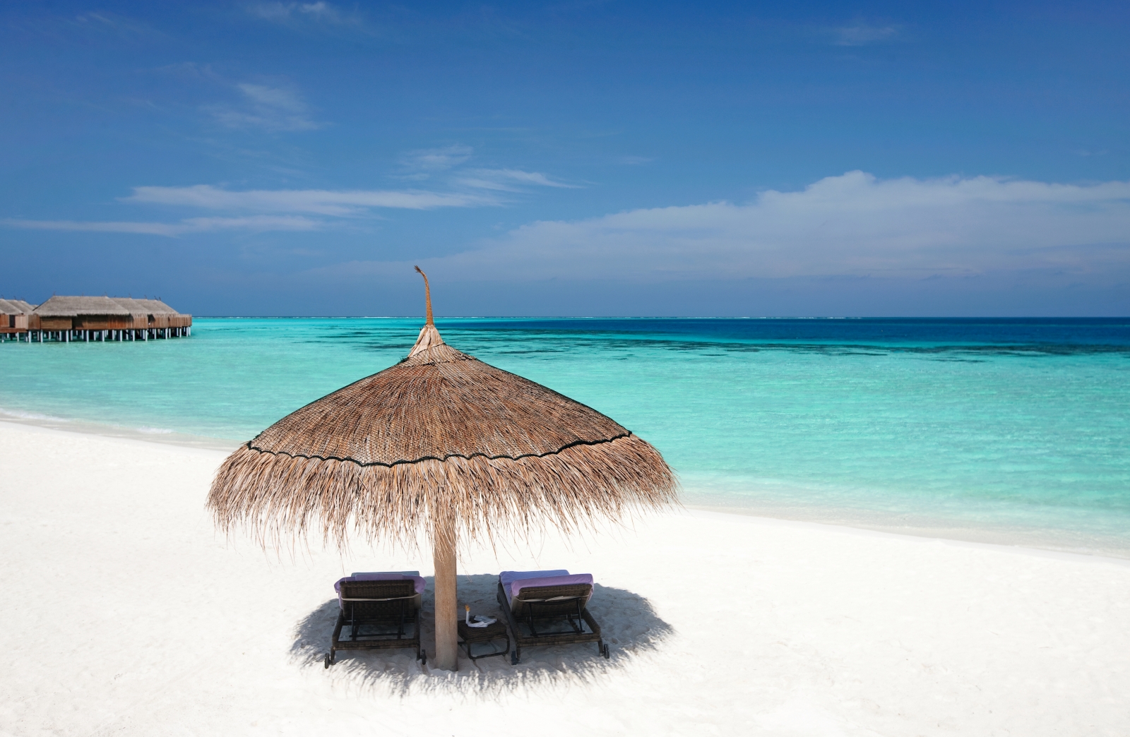 Two sun loungers under a parasol on the white sand beach of luxury resort Constance Moofushi in the Maldives