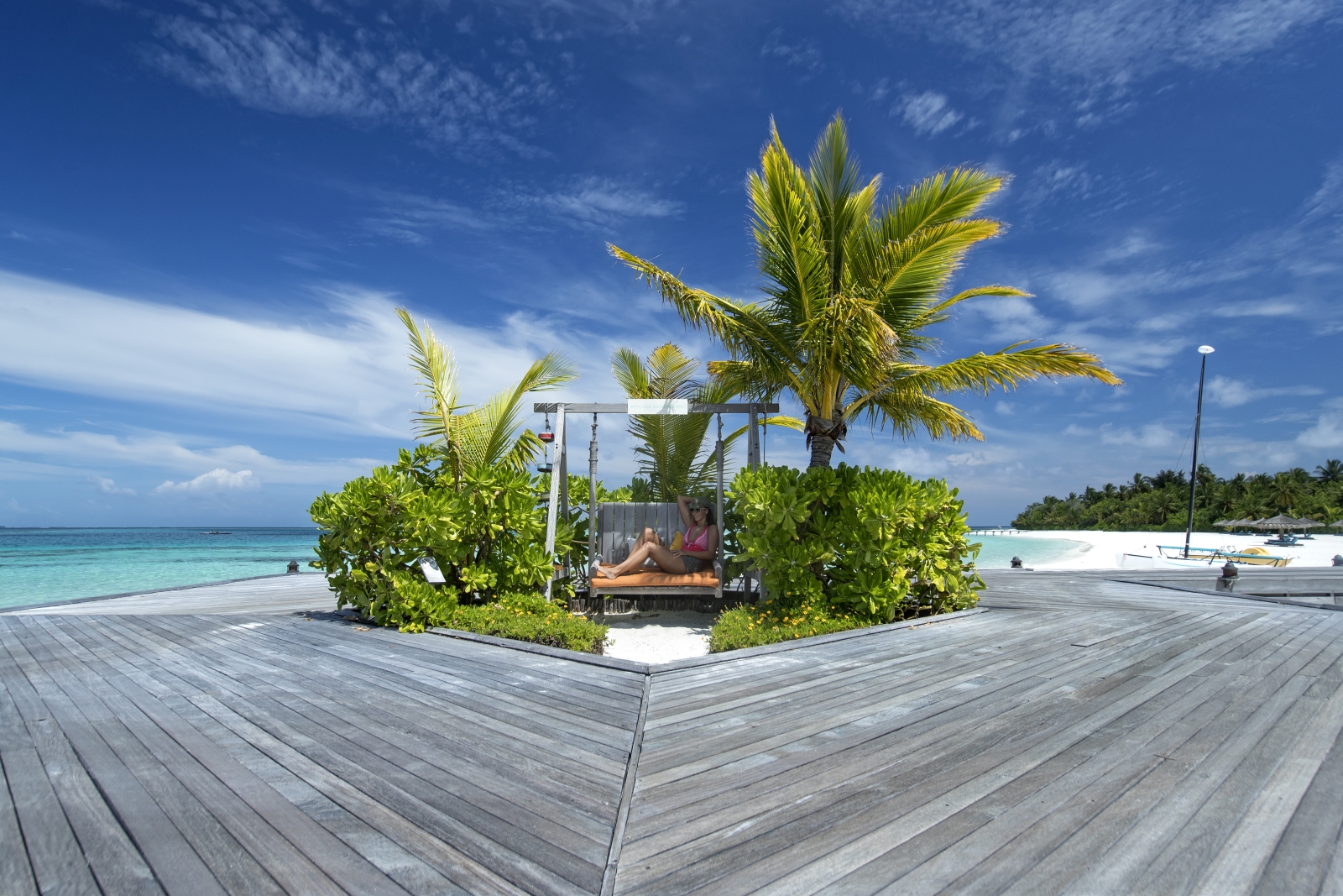 Guest sitting on a wooden swing on the beach of luxury resort Constance Moofushi in the Maldives
