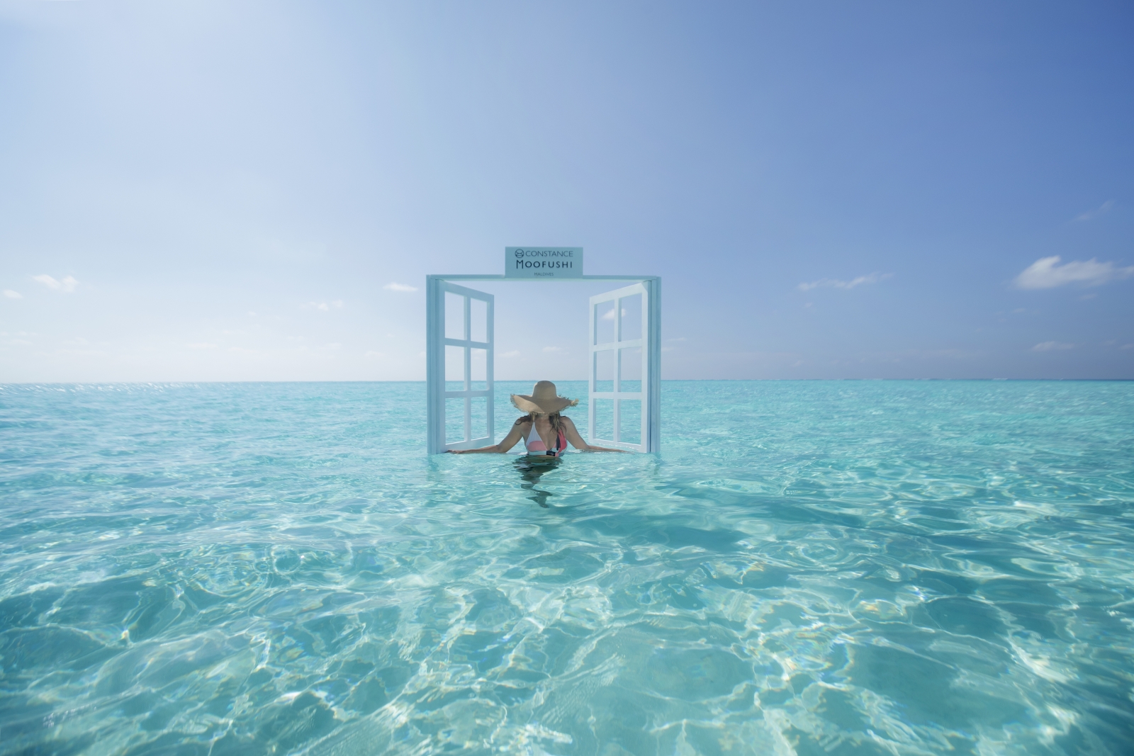 Guest standing in the iconic floating window frame at luxury resort Constance Moofushi in the Maldives