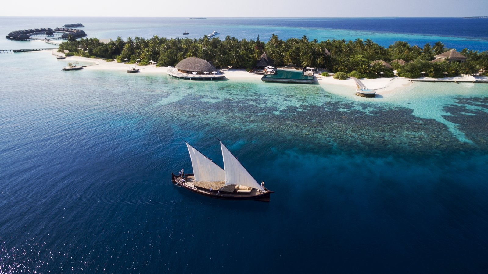 Traditional Dhoni sailing past luxury resort Huvafen Fushi in the Maldives