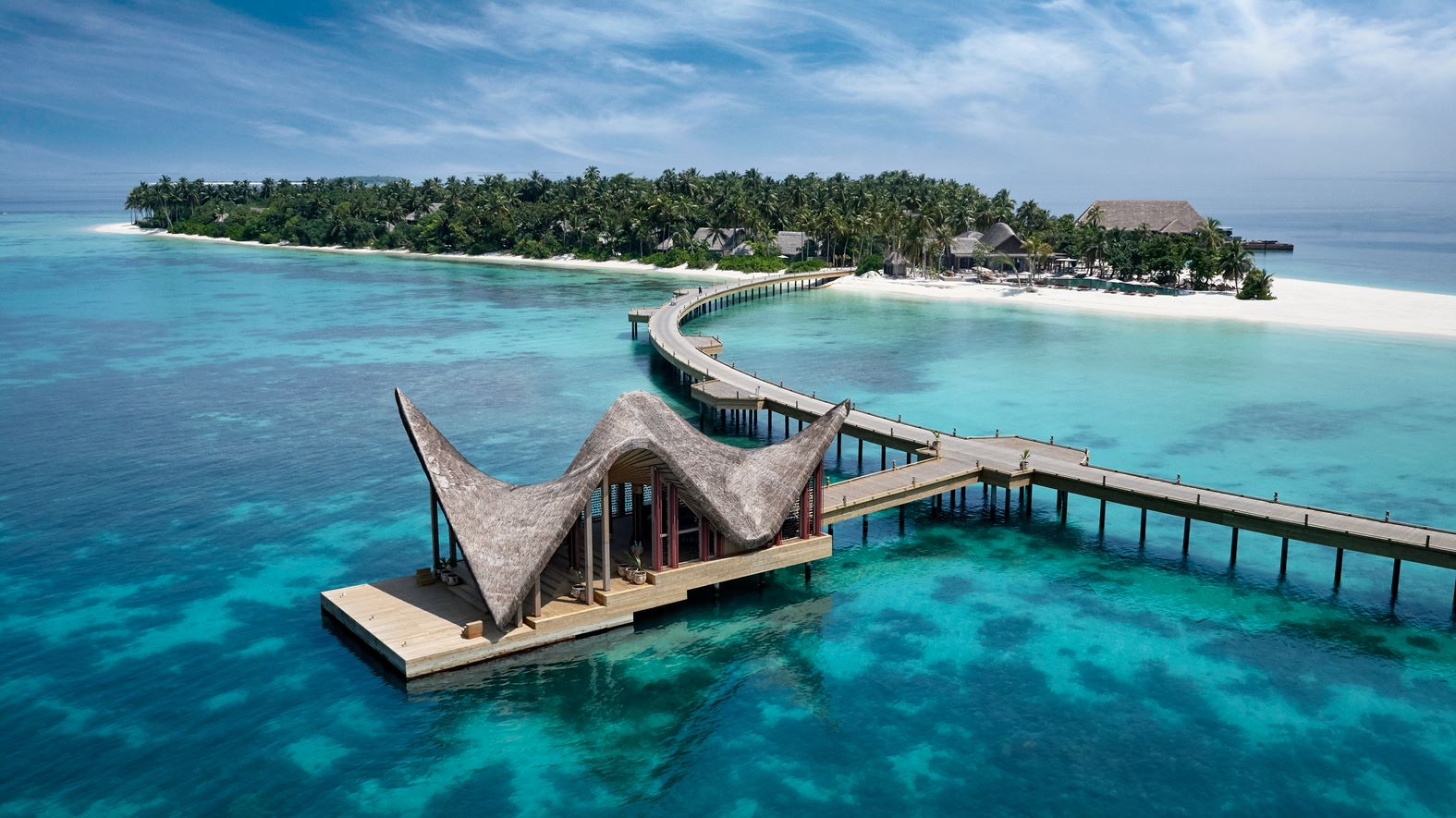 The arrival pier at Joali surrounded by blue water and the island behind