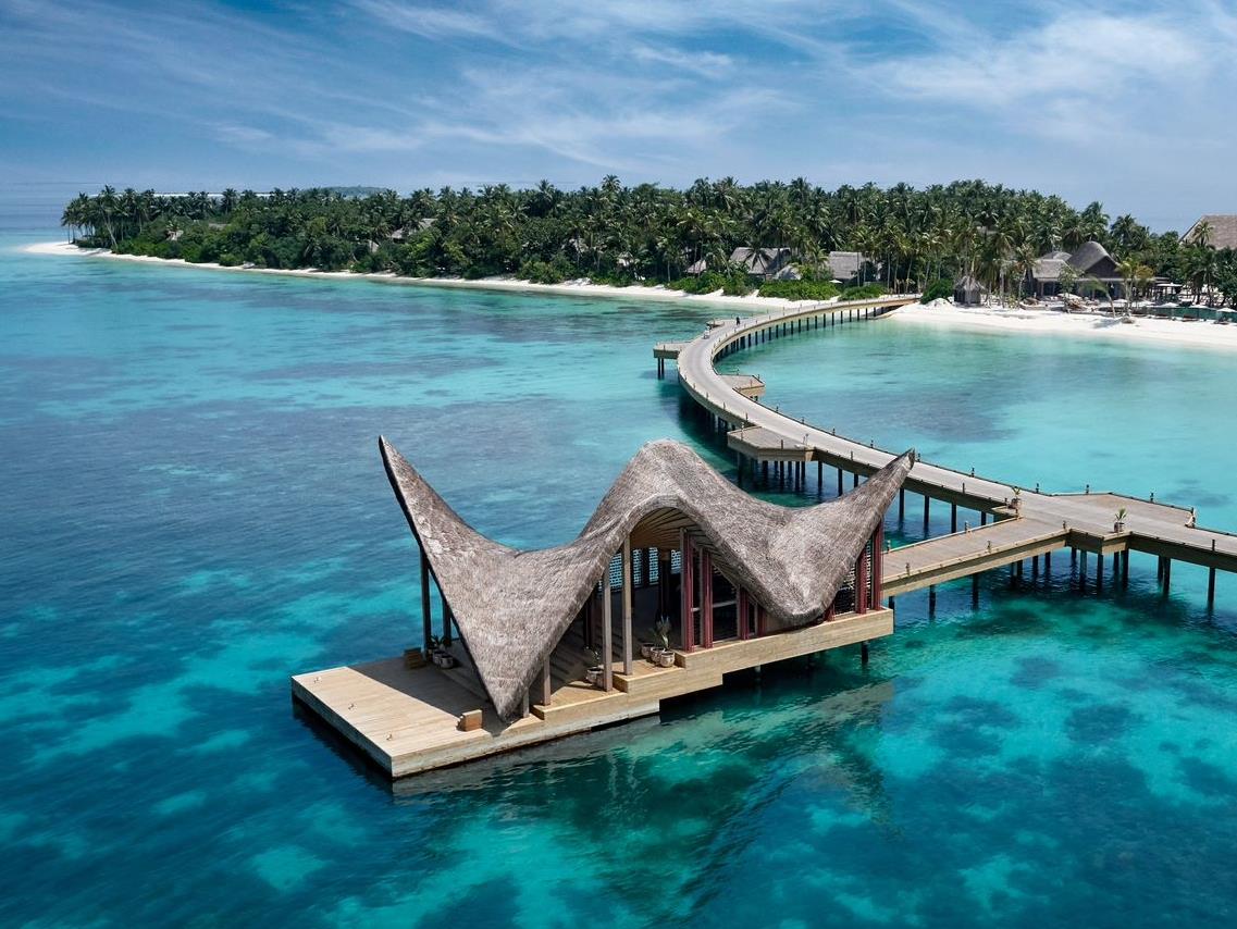 The arrival pier at Joali surrounded by blue water and the island behind