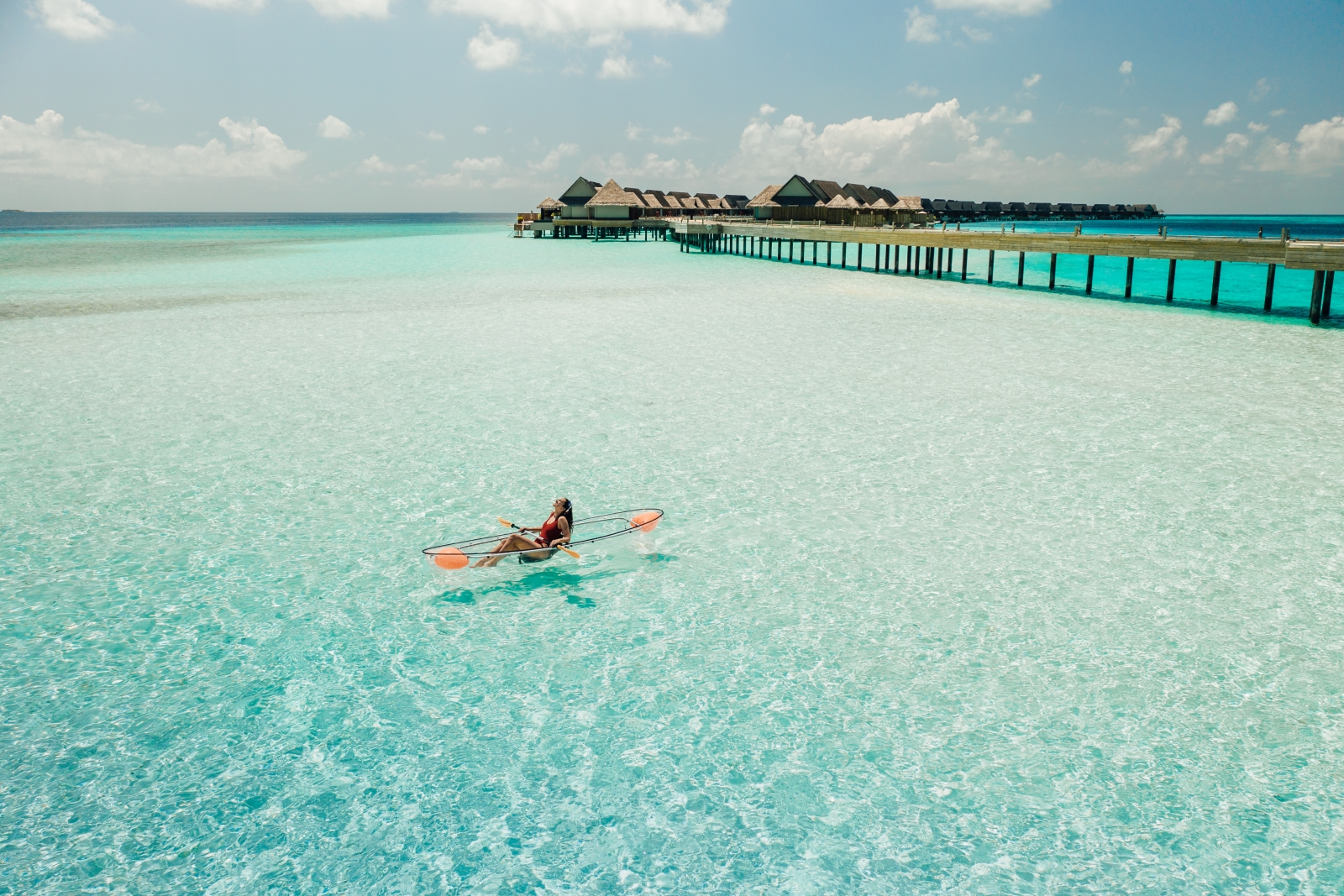 Woman in a see-through kayak paddeling in the turquoise waters of the Indian Ocean at luxury resort Joali in the Maldives