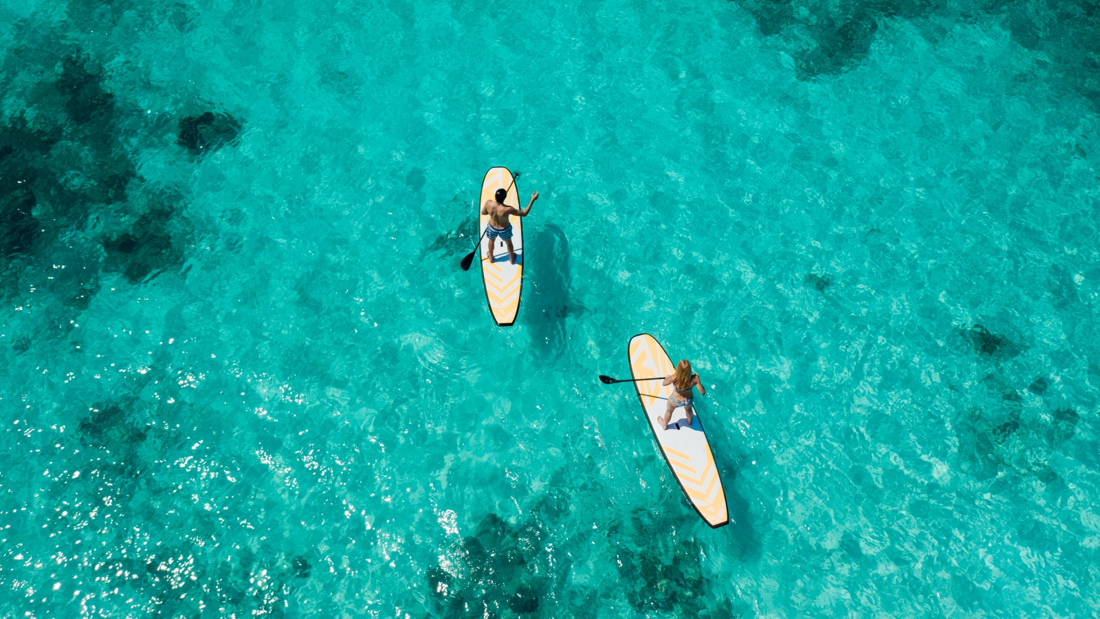 Two guests on stand up paddle boards at luxury resort Joali in the Maldives