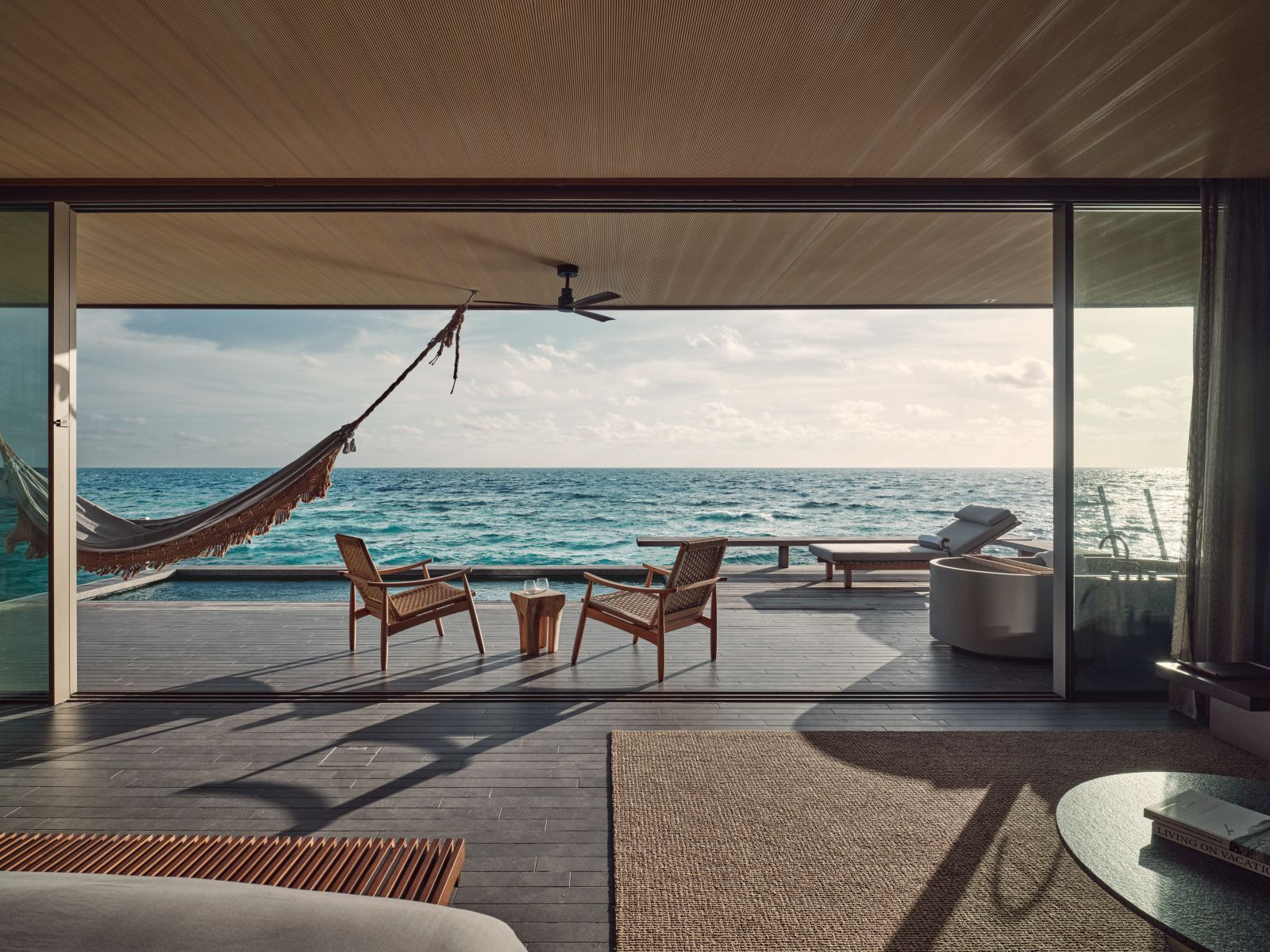 View over the deck with loungers, hammock and chairs, and pool of a water villa at luxury resort Patina in the Maldives