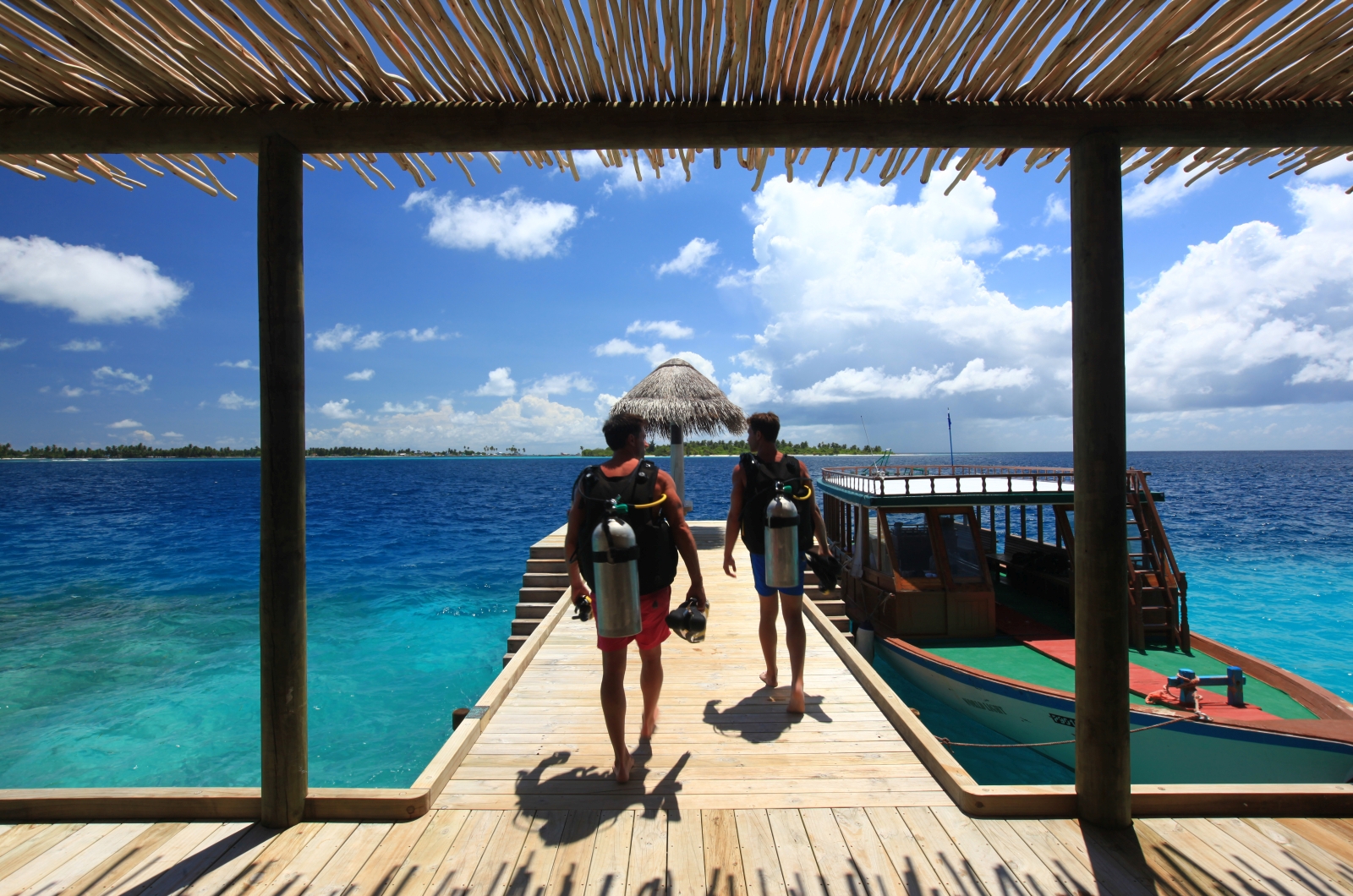 Two divers walk down the jetty in gear at Six Senses Laamu Maldives