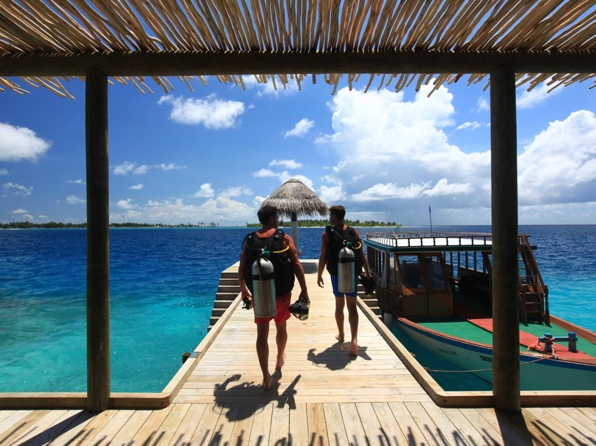 Two divers walk down the jetty in gear at Six Senses Laamu Maldives
