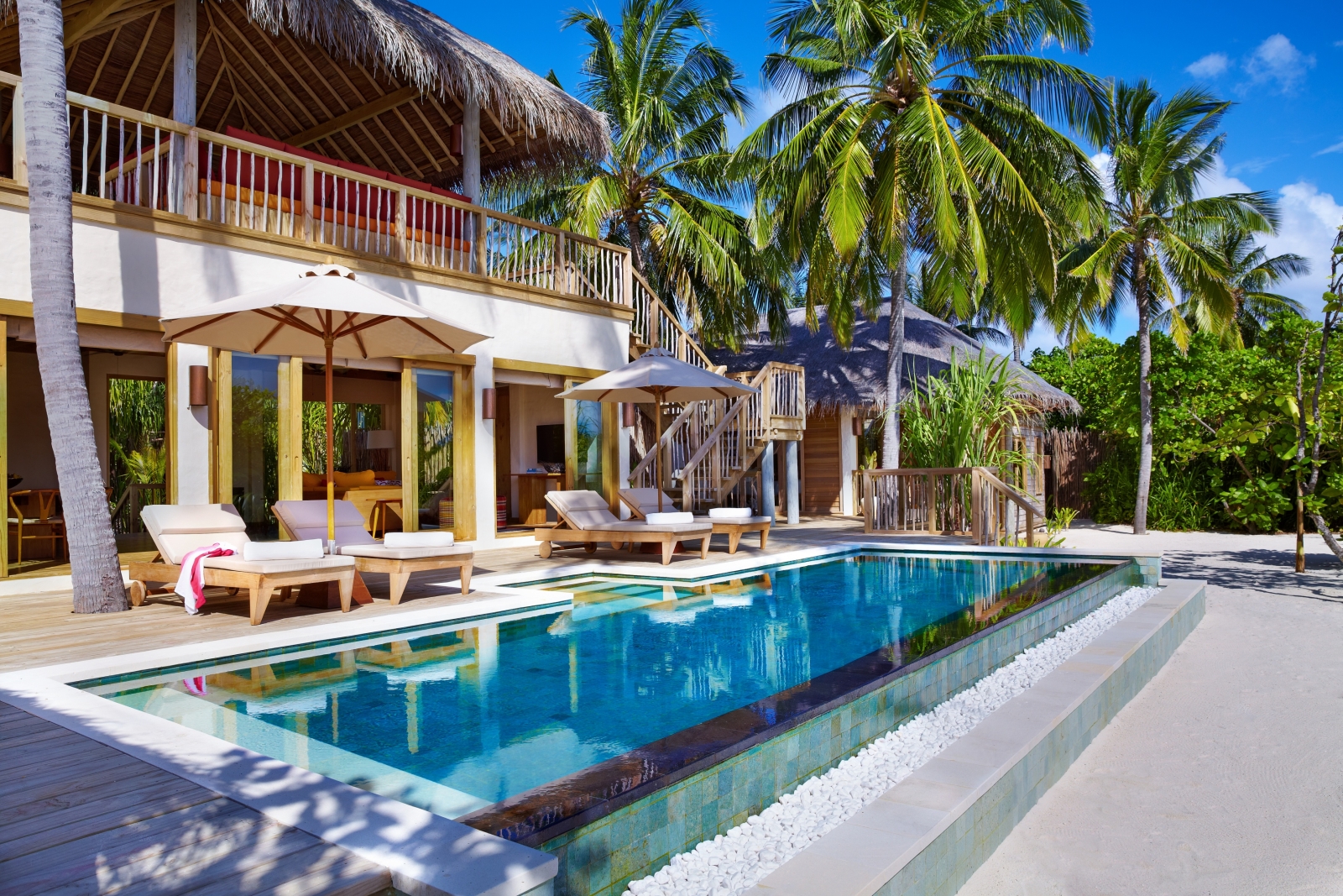 The terrace of a Two-Bedroom Ocean Beach Villa with private pool, loungers and parasols on the palm-strewn white sand beach of luxury resort Six Senses Laamu in the Maldives