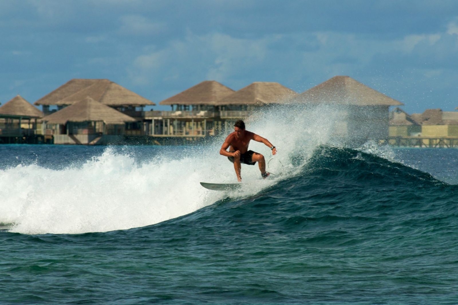 Surfer in front of water villas at Six Senses Laamu