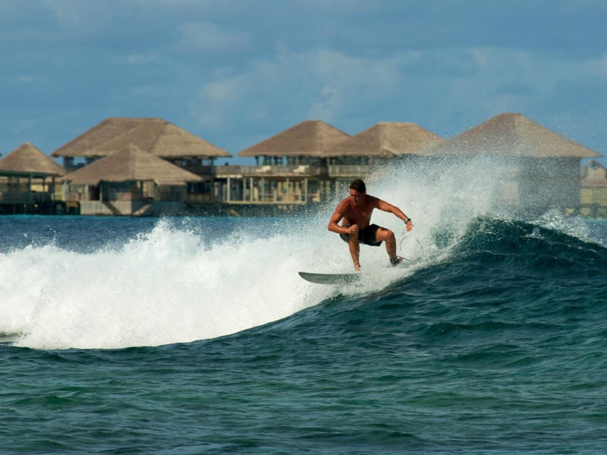 Surfer in front of water villas at Six Senses Laamu
