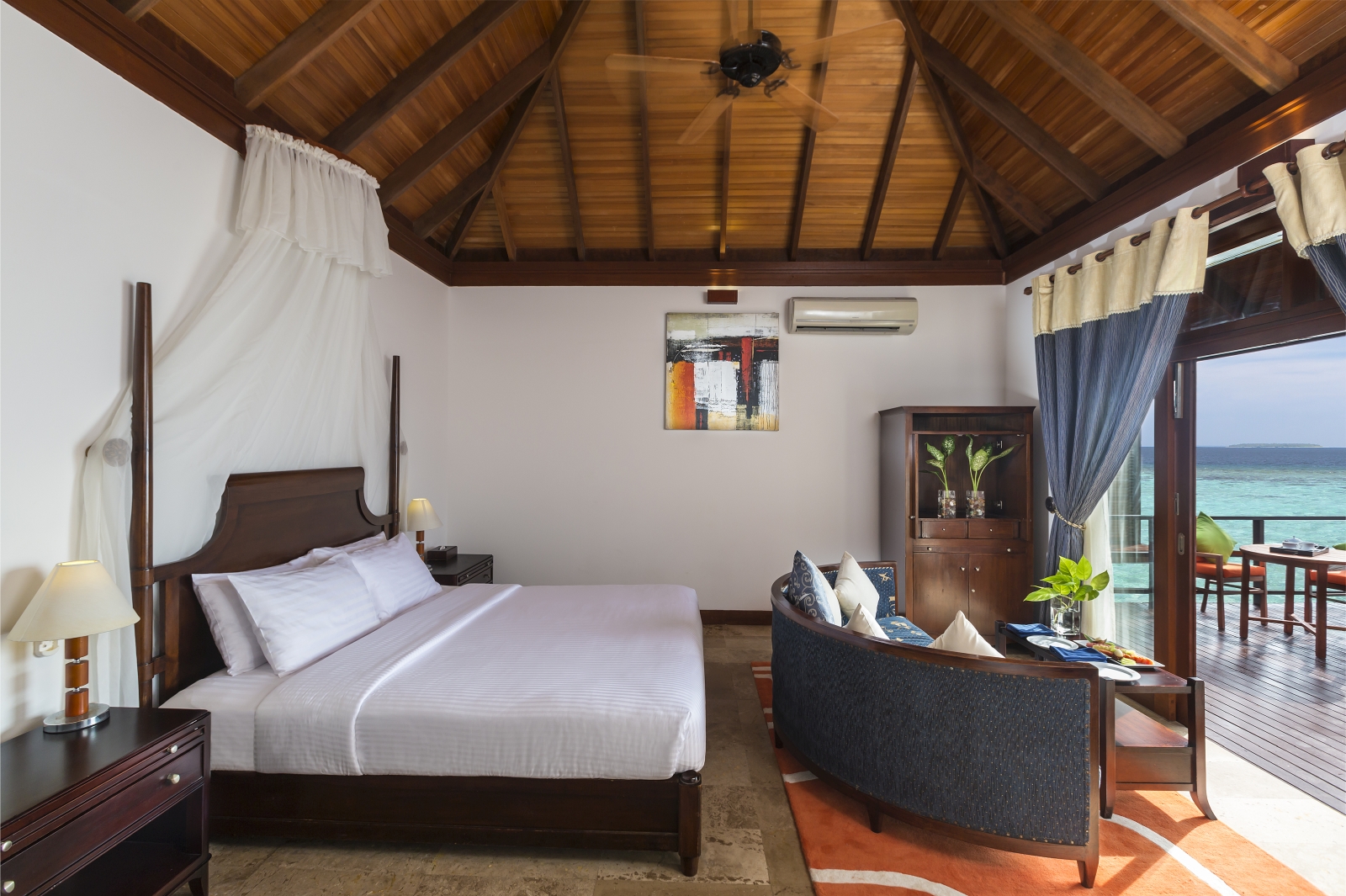Bedroom of a Jacuzzi Water Villa with four poster bed, fan, Air Conditioning and private terrace at luxury resort Sun Siyam Olhuveli in the Maldives