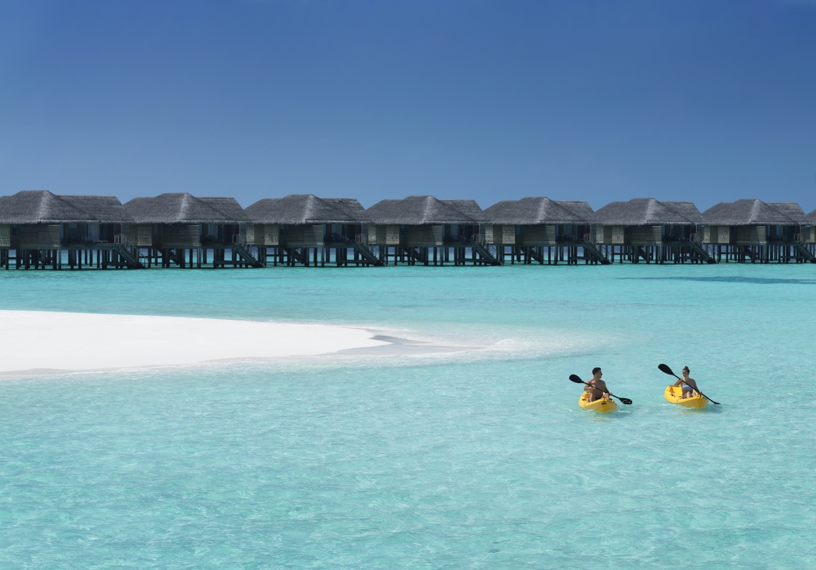 Couple kayak on clear water in front of the overwater villas