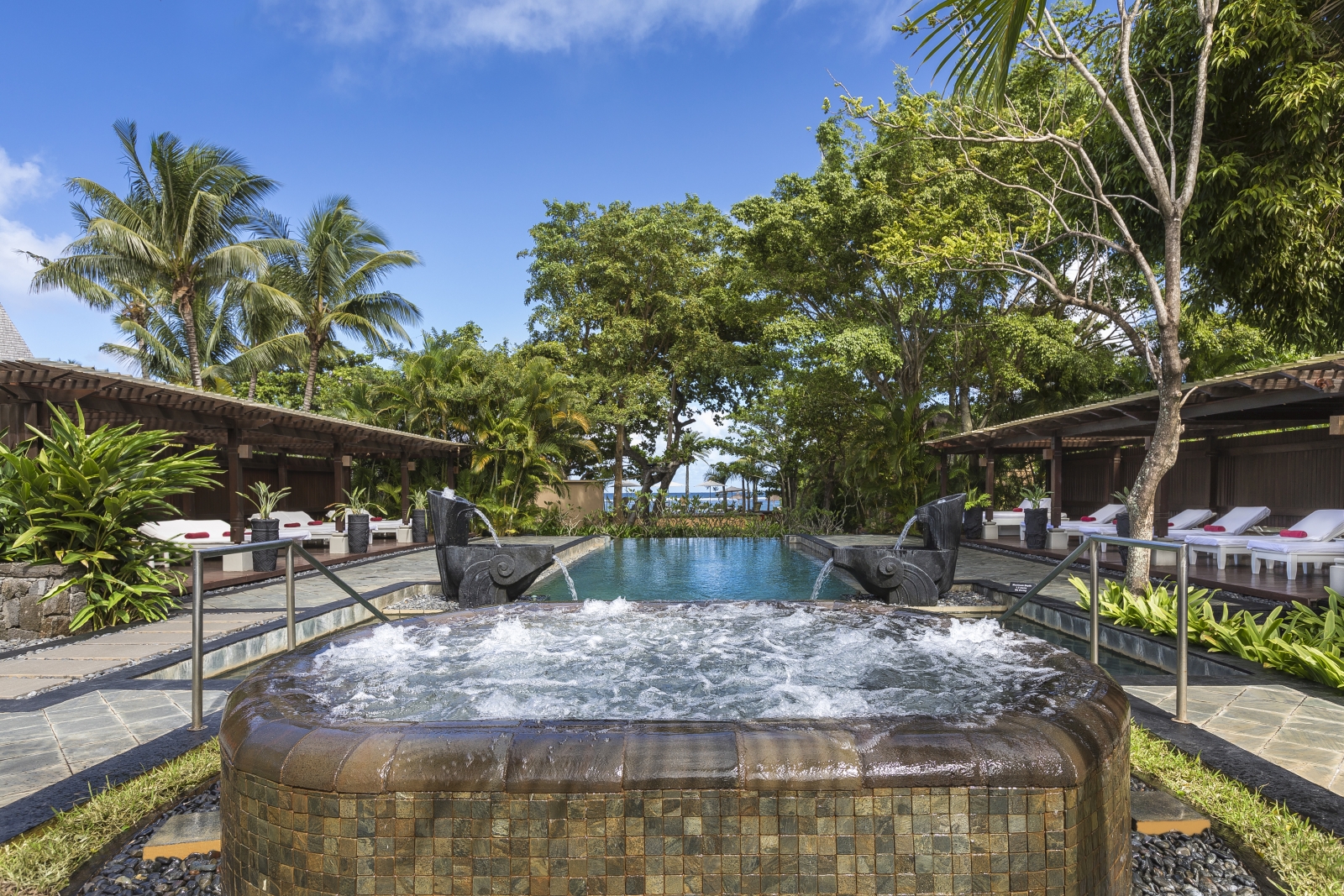 The jacuzzi and pool at the Spa of Shanti Maurice, lined with loungers and palm trees