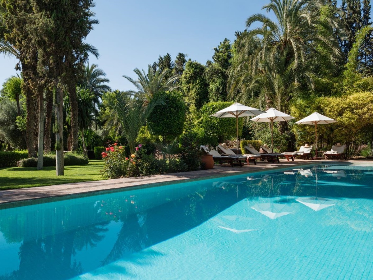 The pool, set in lush green gardens, with sunbeds and sun umbrellas at Dar Zemora in Morocco