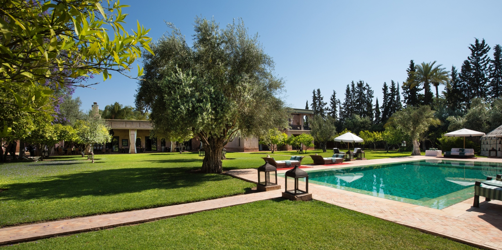 Garden and pool area with sun loungers, umbrellas, trees and lanterns at Ezzahra in Marrakech, Morocco
