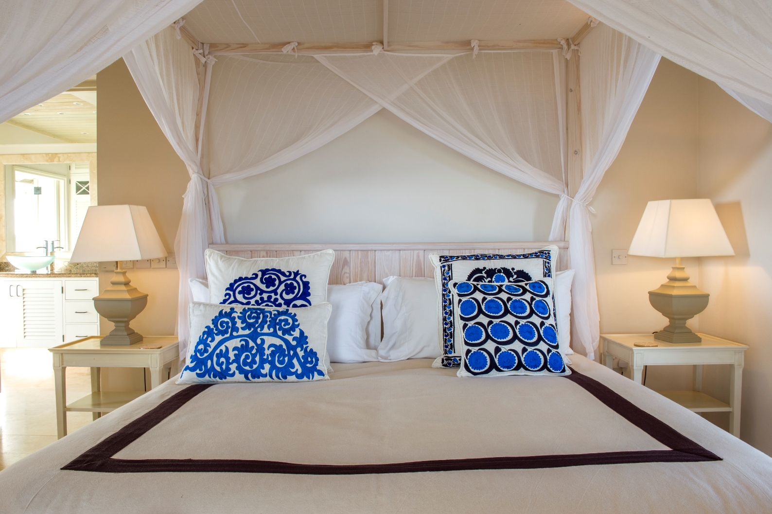 a double bed with blue cushions and mosquito nets at luxury villa Pangolin in Mustique