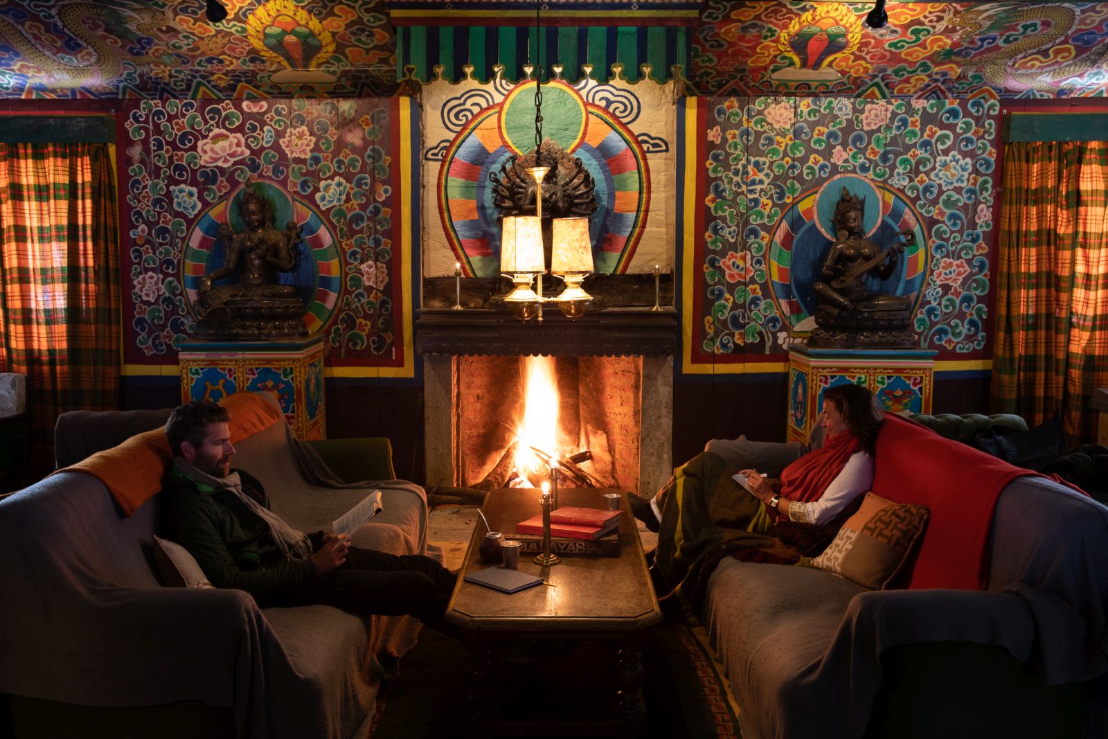 Two people sitting by a glowing fireplace reading books