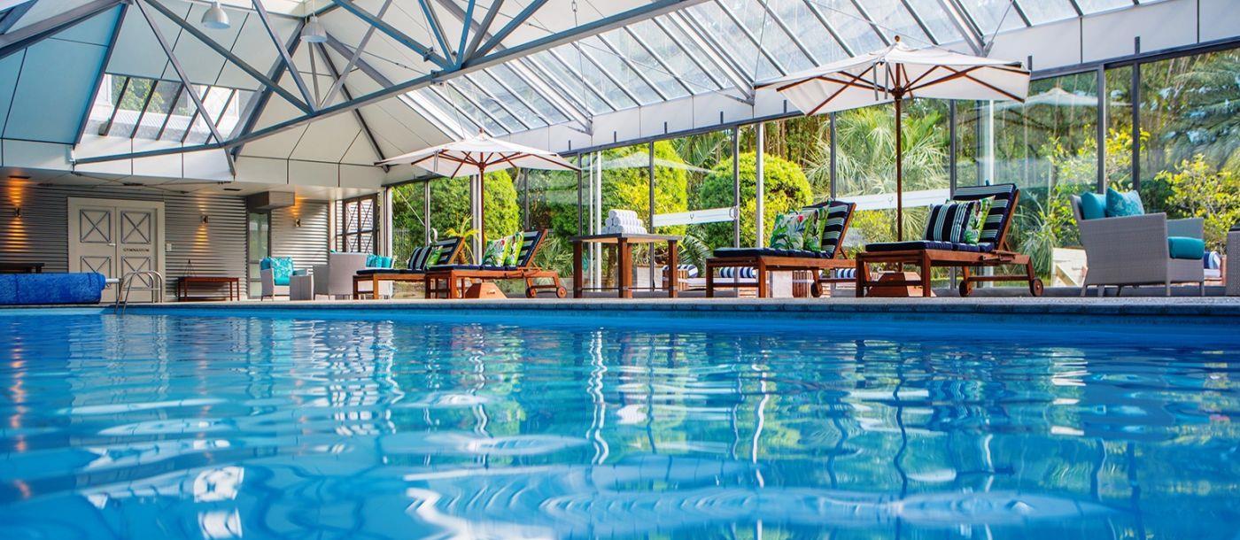 The swimming pool with sunbeds, chairs and tables in the covered spa at Wharekauhau luxury lodge in New Zealand