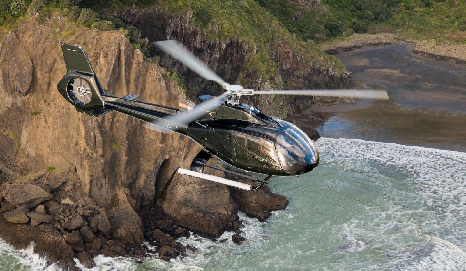 The Landing New Zealand helicopter flying over the cliffs and bay
