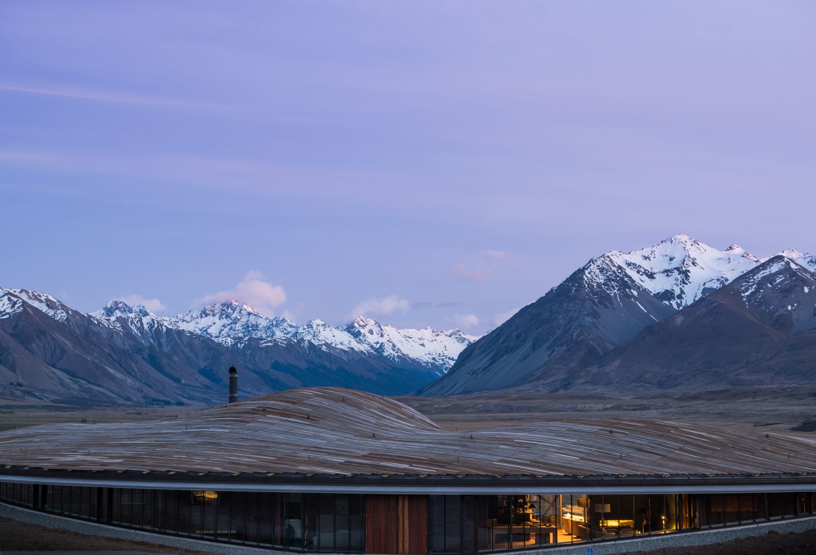 Exterior shot of the sweeping roof that blends in with the mountains in the background of The Lindis Lodge in New Zealand