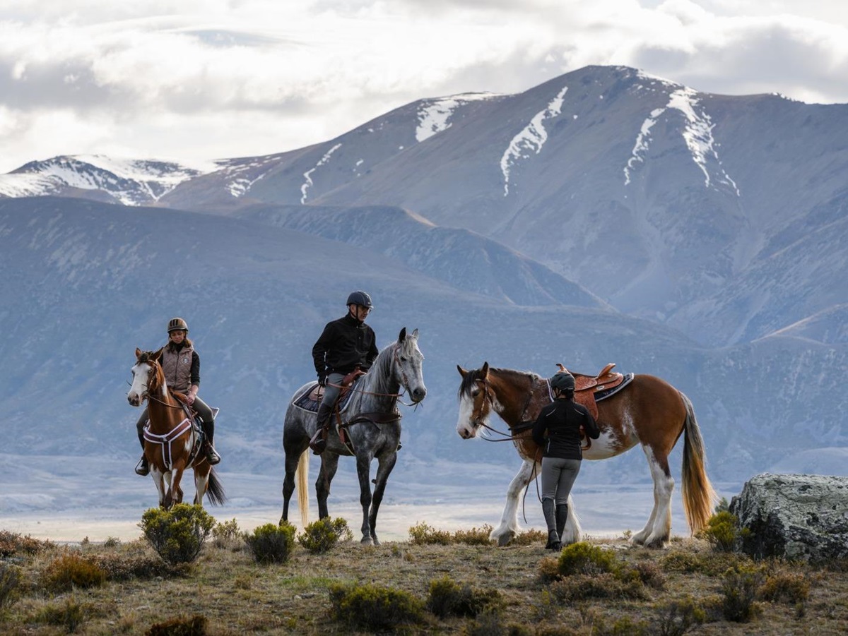 Two people sat on horses and one person holding a horse in the mountains at The Lindis Lodge in New Zealand