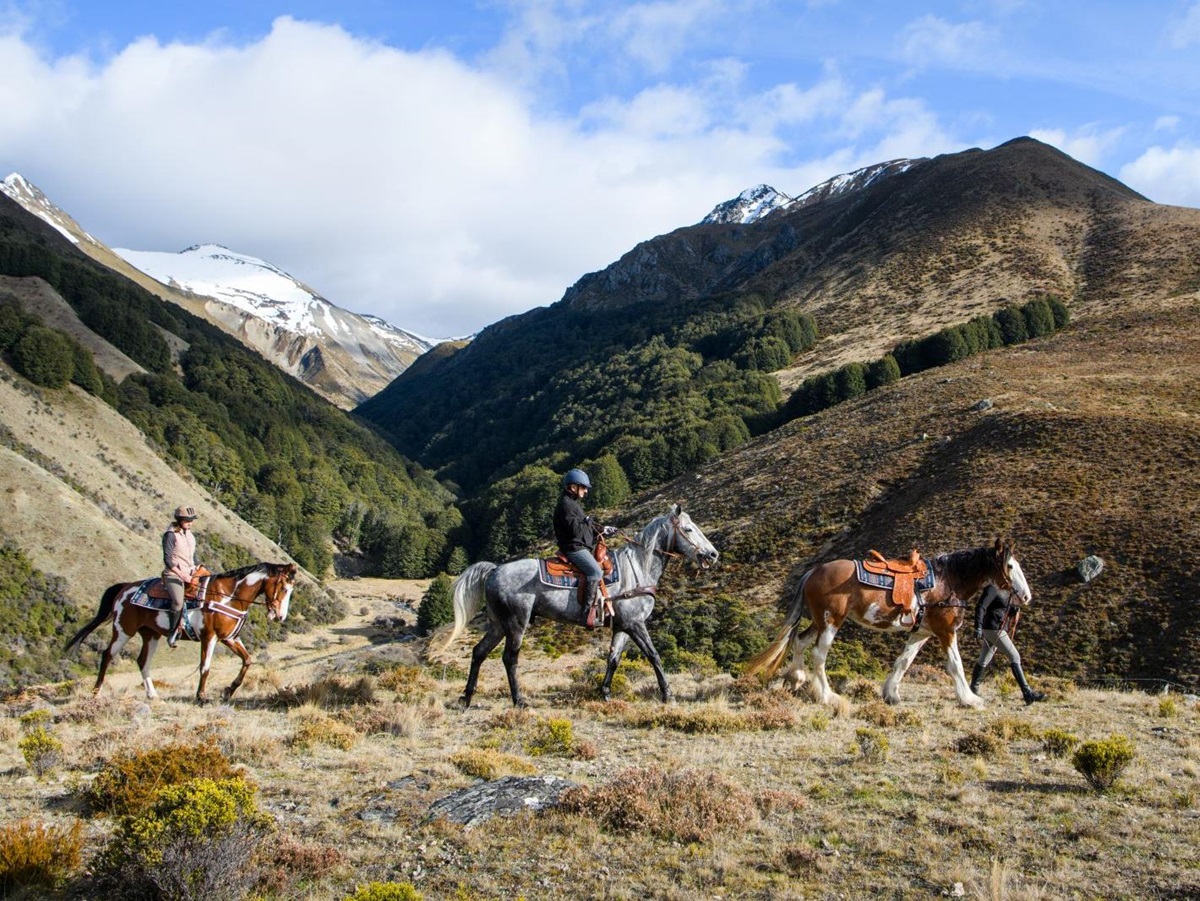 Two people riding and one person leading a horse across the mountains at The Lindis Lodge in New Zealand