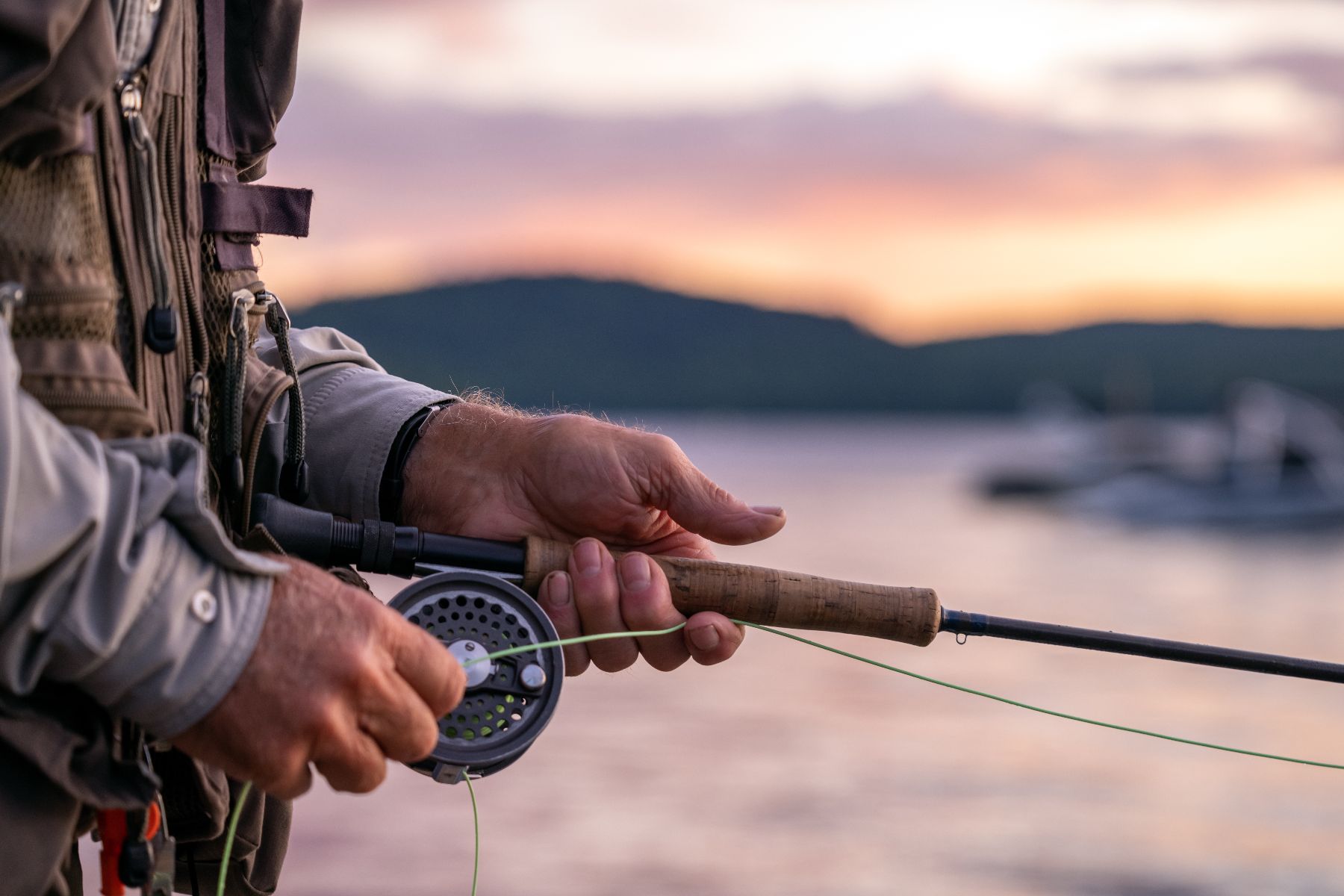 Close-up of a fisherman winding a fishing rod reel against a lake backdrop