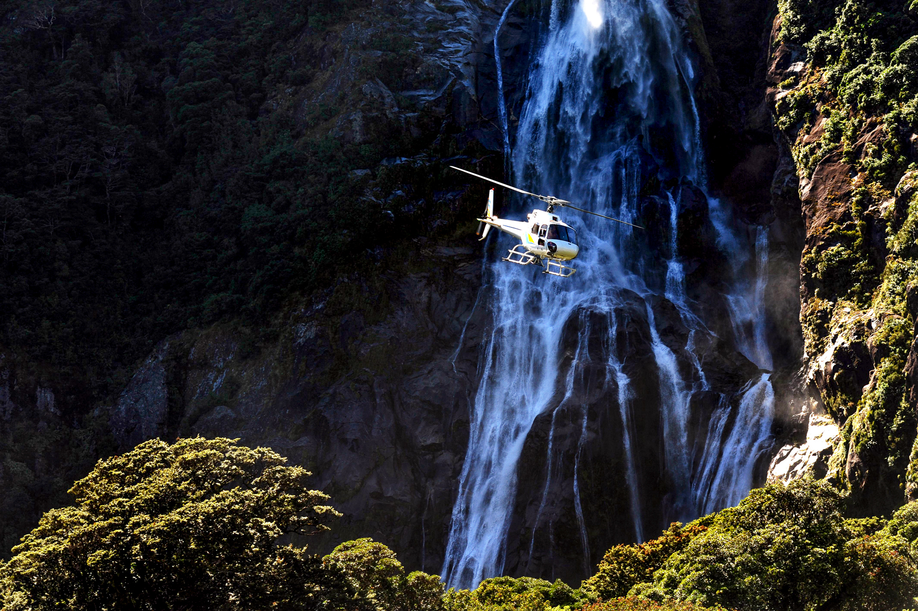 A helicopter flying past a waterfall at Milford Sound