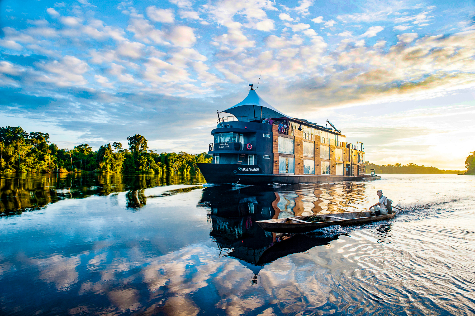 A canoe sailing past the Aria Amazon luxury river cruiser in Peru