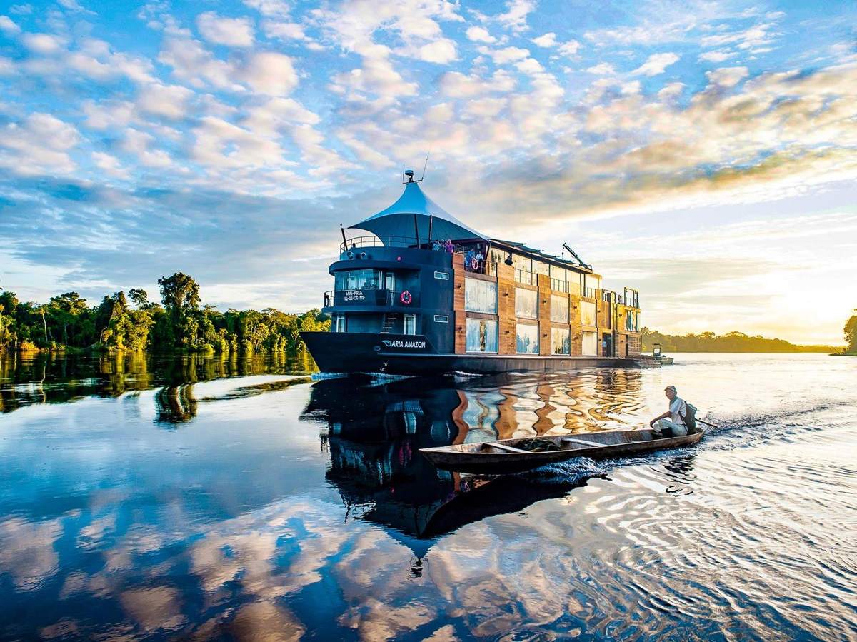 A canoe sailing past the Aria Amazon luxury river cruiser in Peru