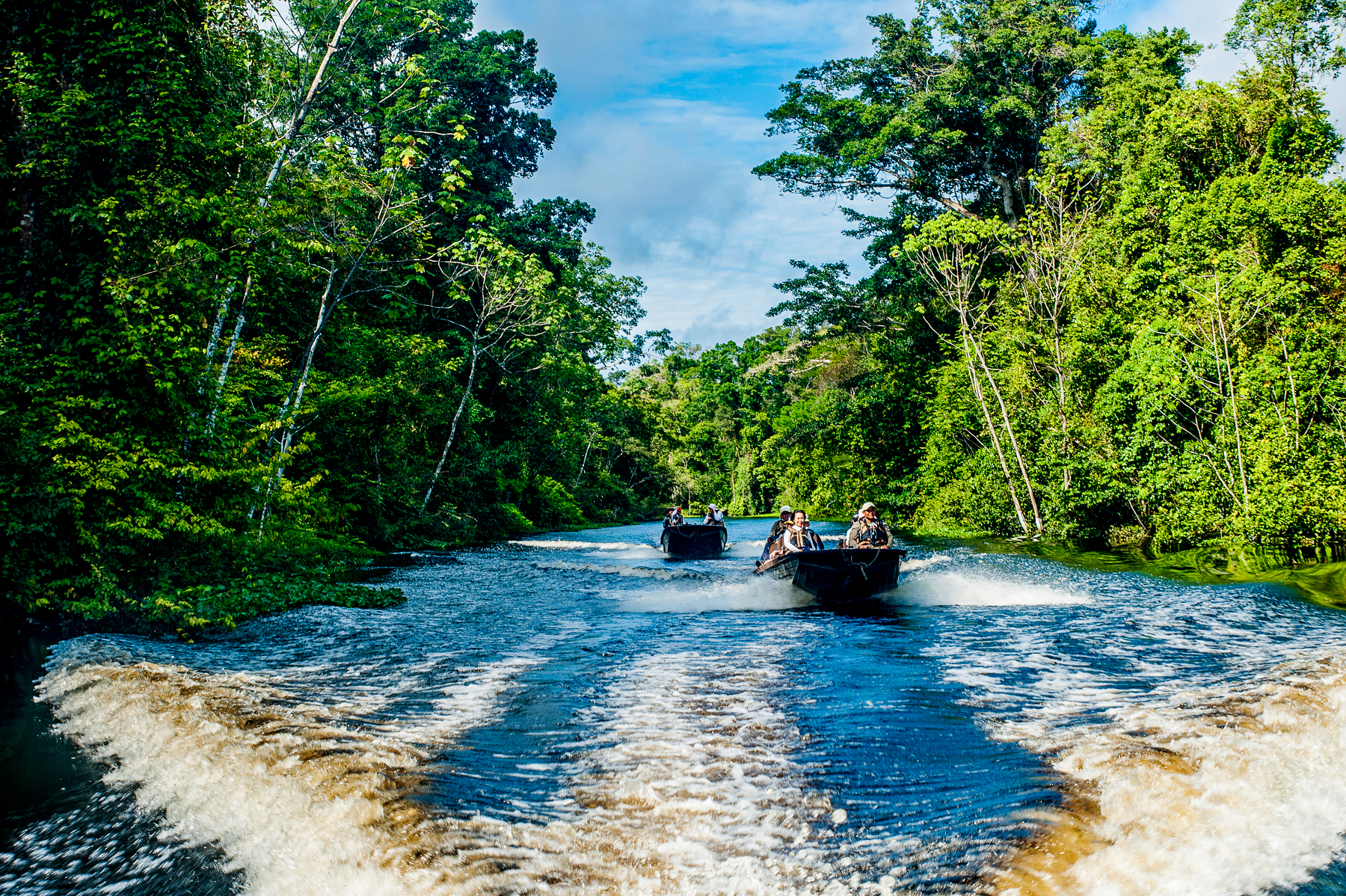 Skiffs sailing across a canal from the Aria Amazon luxury river cruiser in Peru