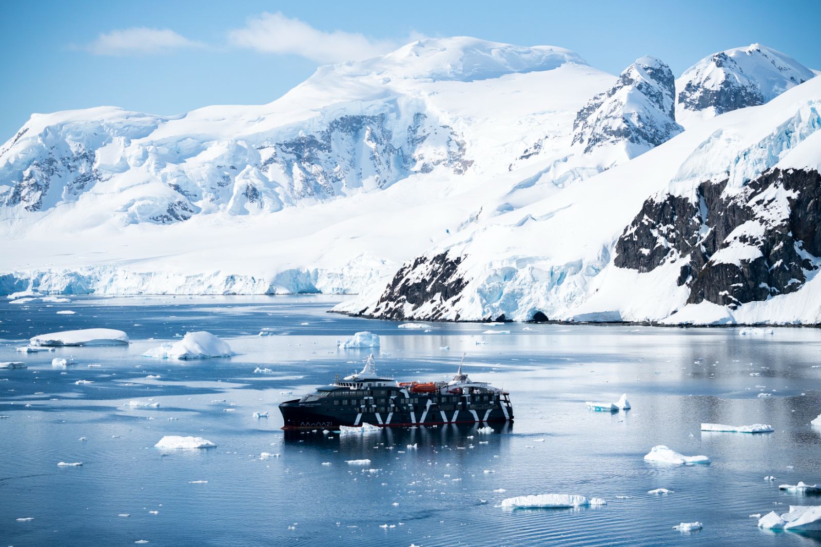 The Magellan Explorer against a backdrop of Antarctic mountains