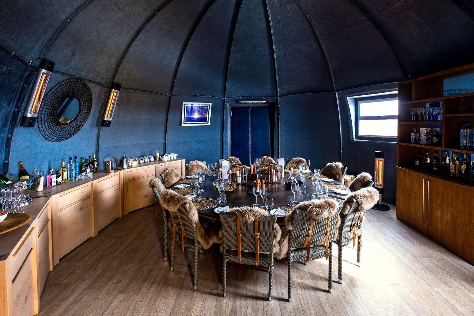 Camp dining table set with plates and glasses, with fur blankets over the chairs