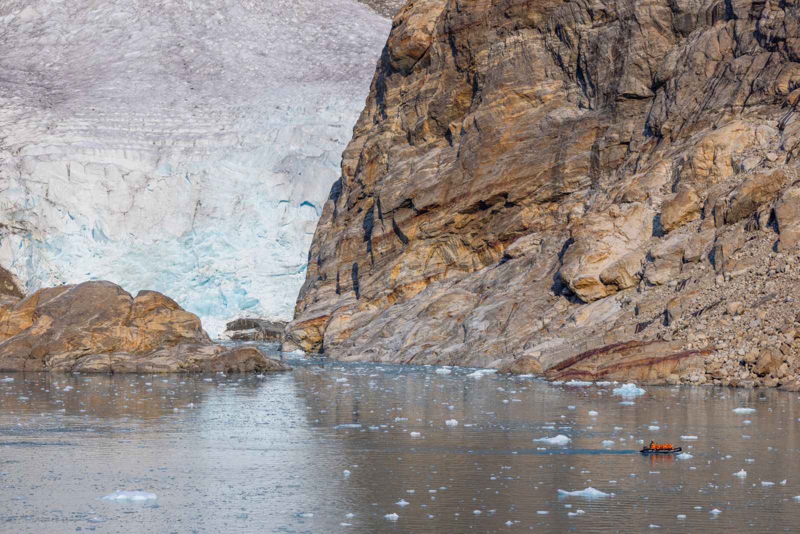 A Zodiac boat in the waters beneath a colossal glacier in Greenland